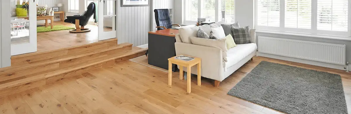 A modern living room with professionally installed laminate flooring, a beige sofa, a small side table, a gray rug, and large windows with white shutters in Toledo, OH